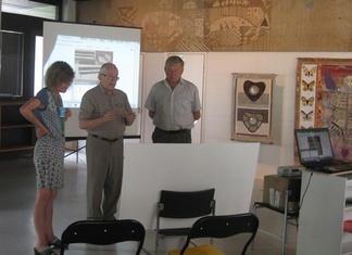 TATSI2014-tapahtuman järjestäjä Soile Kinnunen, sisustusarkkitehti Risto Halme ja Nälkälinnanmäki-Seuran puheenjohtaja Matti Kosonen tutustumassa havaintoaineistoon ennen Halmeen esitelmän alkua vanhan kirjaston Akvaario-salissa. Taustalla Oili Mäen täkänän alla Kaiju Haanpään tekstiilejä. 